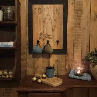 Sfeerfoto van houten wand kopjeshouder met drie zwarte haken en sfeervolle koffieprint